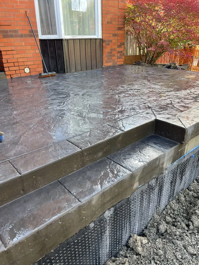 Slate-textured stamped concrete porch and steps against a brick house, coloured and sealed