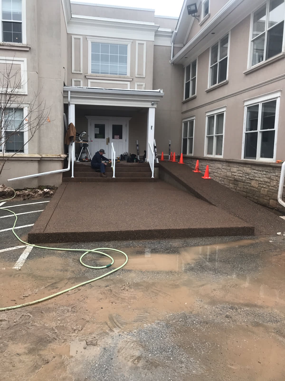 Brown coloured concrete apron with a broadcast-aggregate finish and a barrier-free ramp at a building entrance