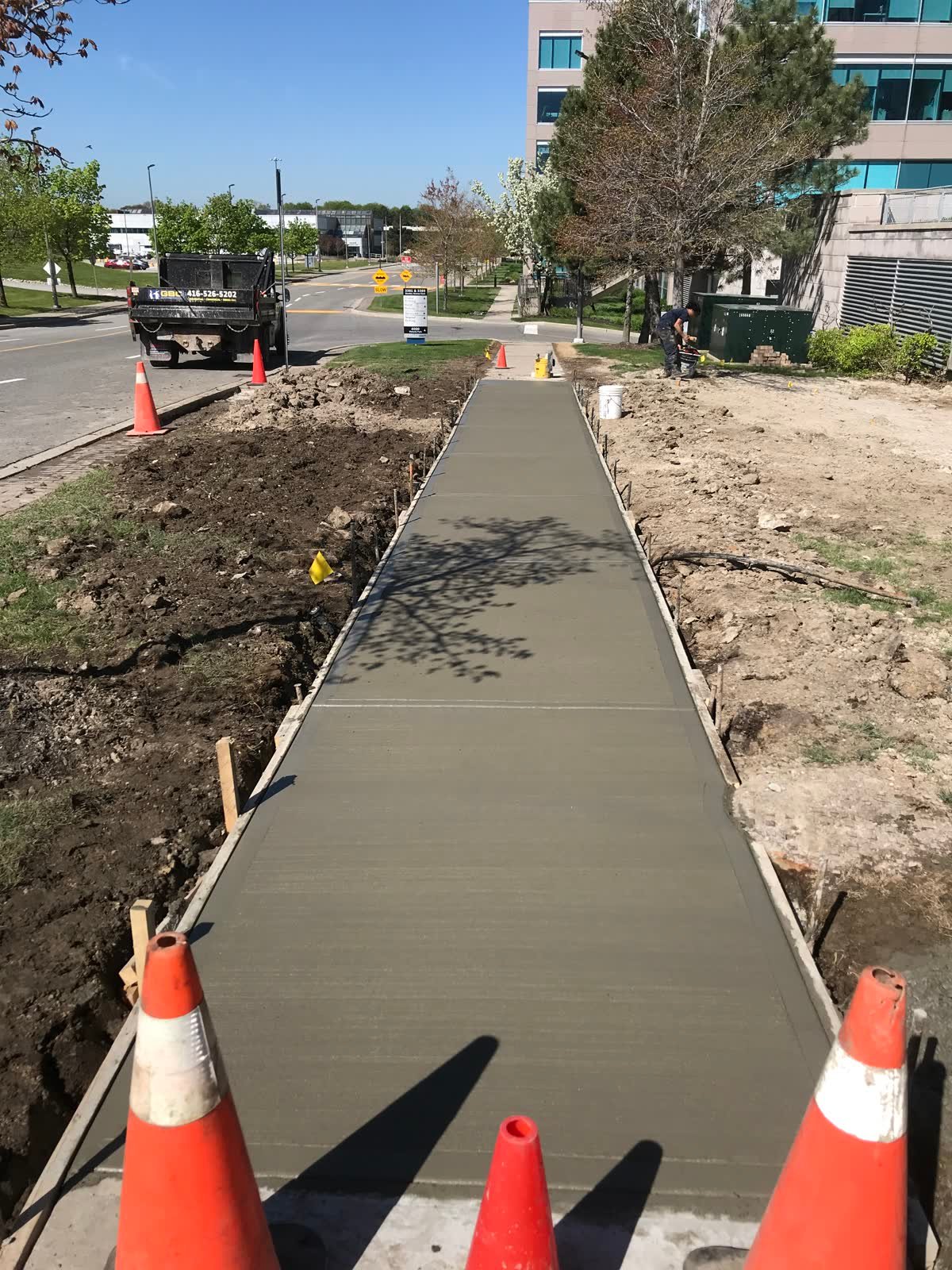 Long freshly poured broom-finished concrete walkway with timber forms, running through an office park
