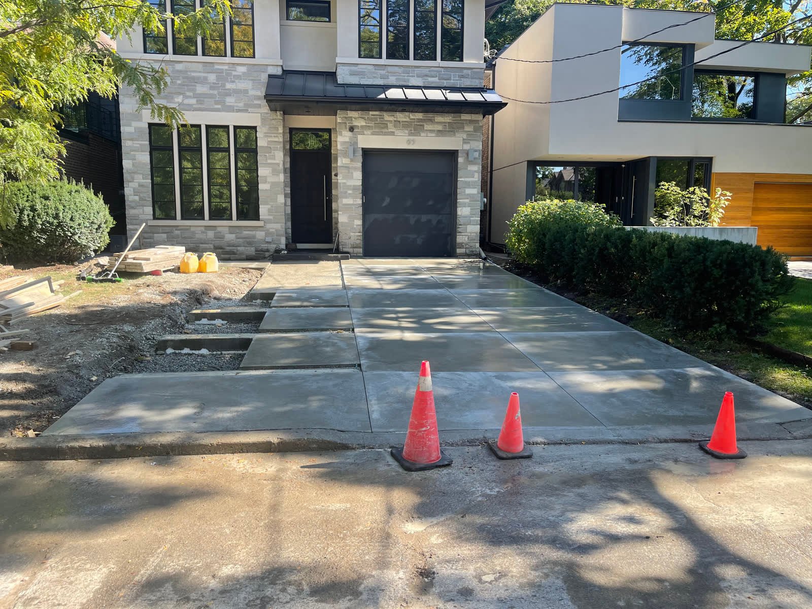 Wide smooth-finished concrete driveway with a saw-cut grid pattern in front of a modern stone house