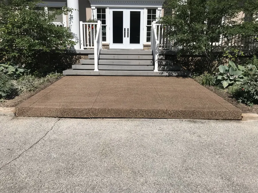 Tan-coloured concrete entry landing with an exposed-aggregate border at the base of front steps