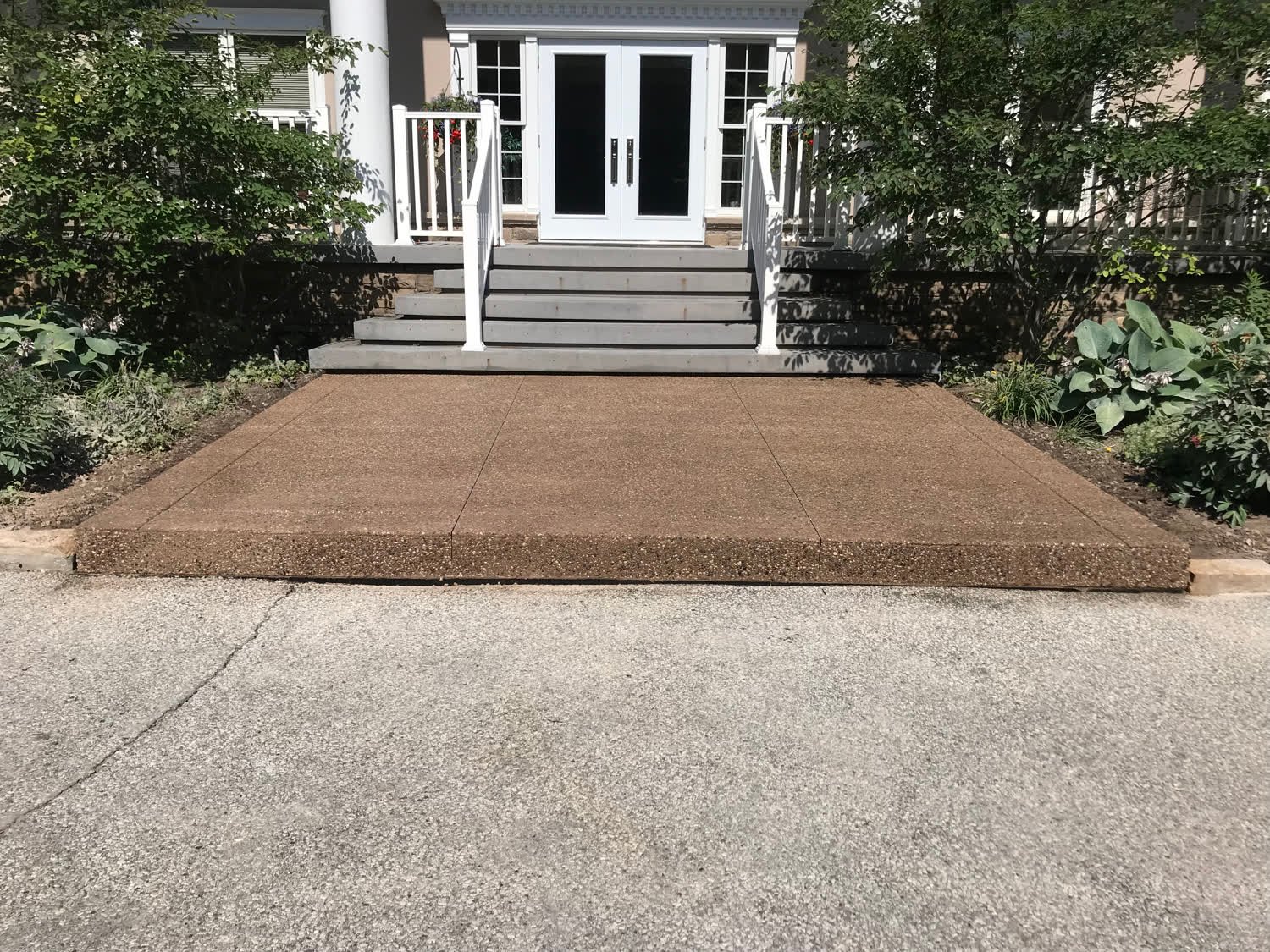 Tan-coloured concrete entry landing with an exposed-aggregate border at the base of front steps