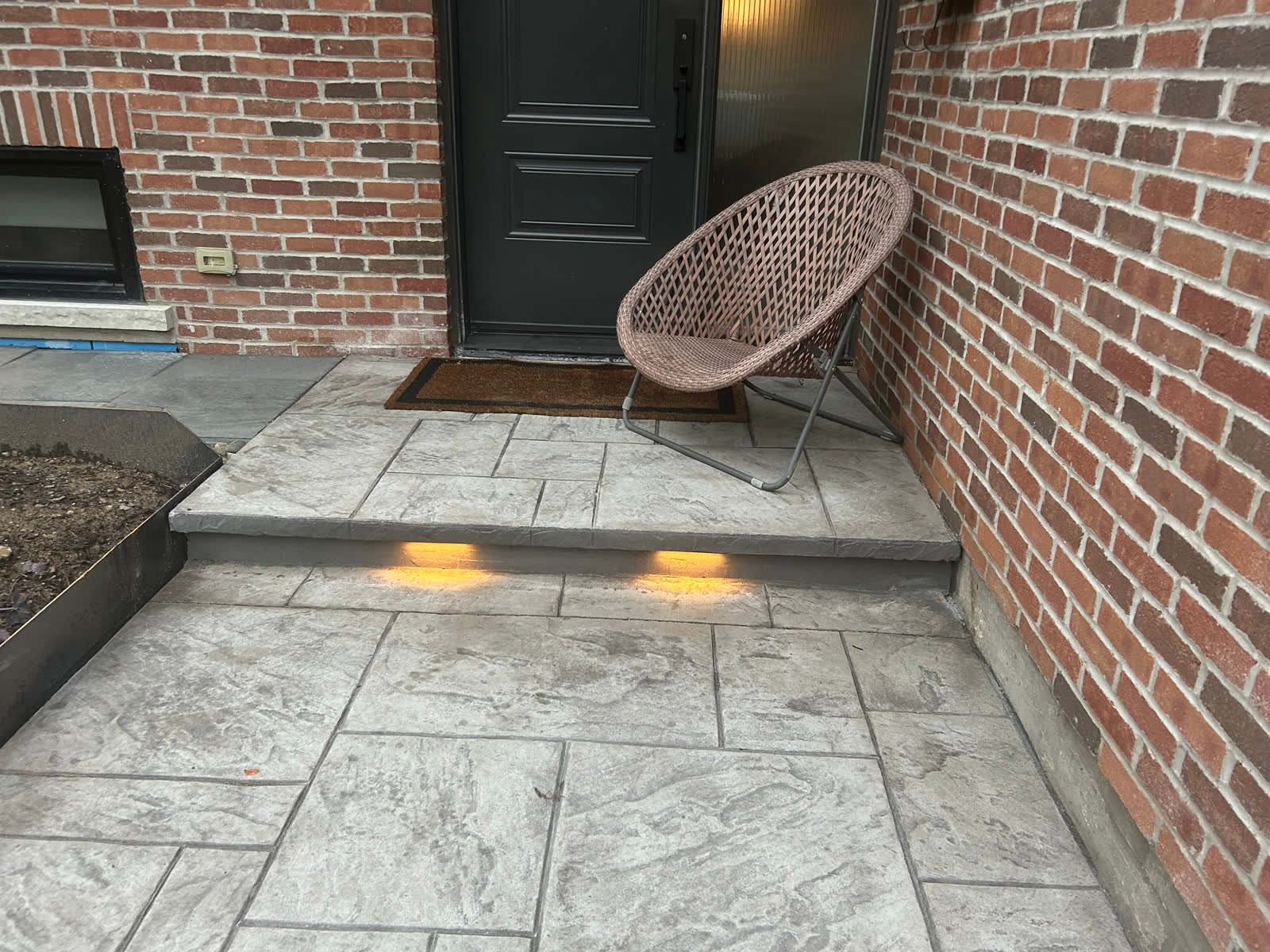 Grey ashlar-stamped concrete entry porch and step with an LED light in the riser, beside a brick wall