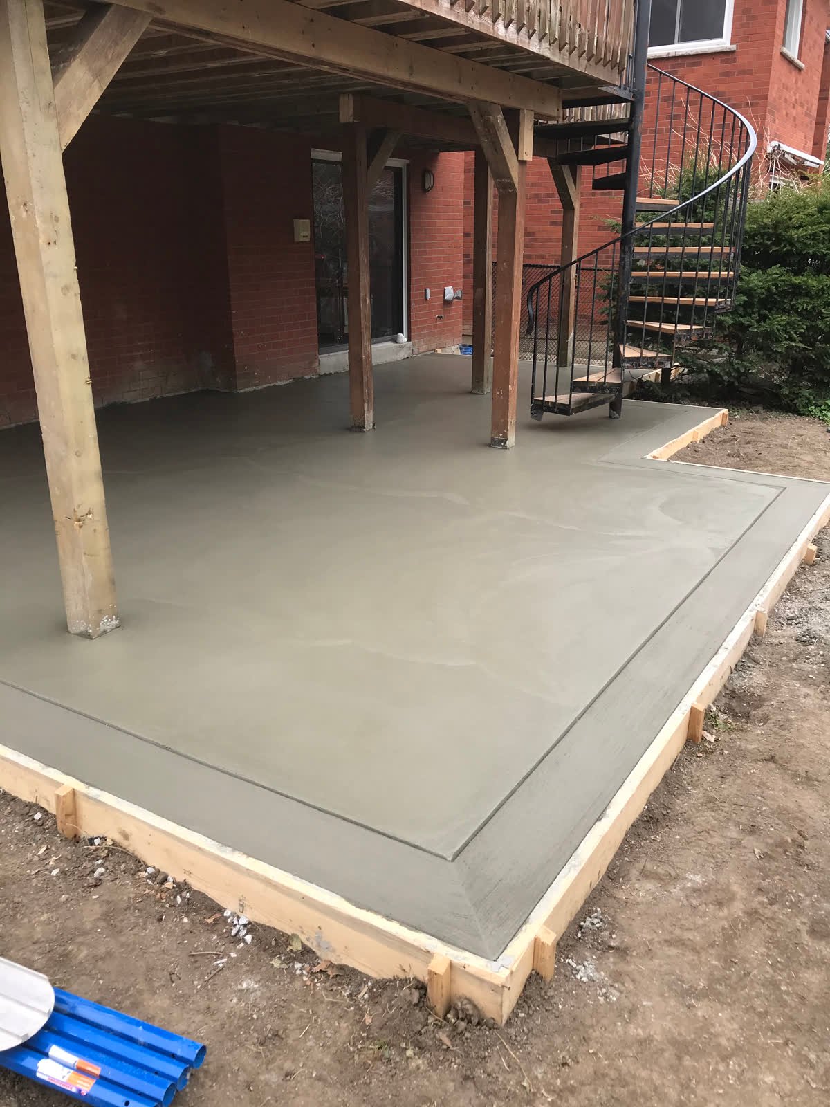 Freshly finished smooth concrete patio with a tooled border edge, poured under a raised wood deck