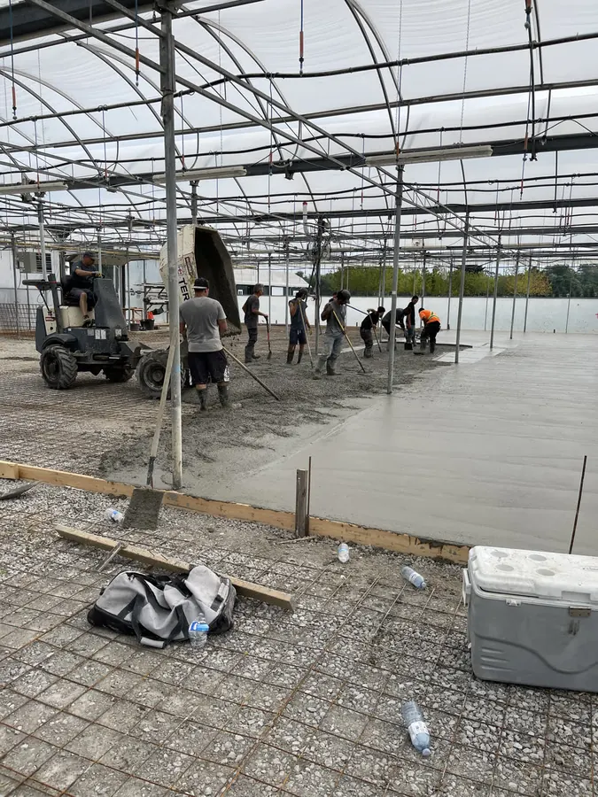 Crew of workers placing and screeding a large reinforced concrete floor slab inside a greenhouse