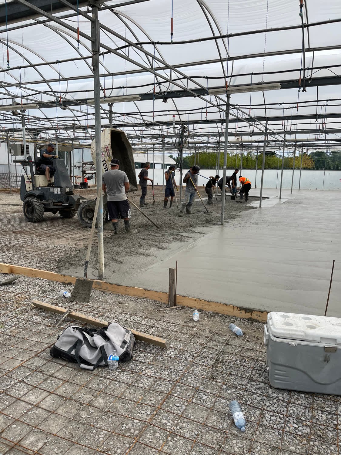 Crew of workers placing and screeding a large reinforced concrete floor slab inside a greenhouse