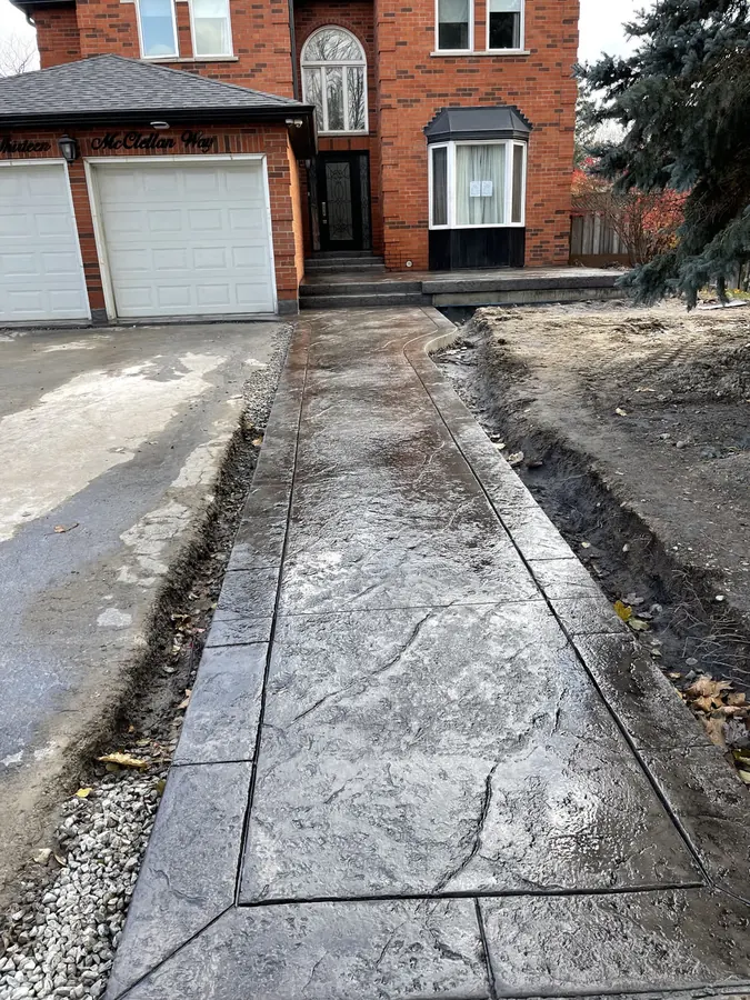 Grey random-stone stamped concrete walkway with a banded border curving from driveway to front door