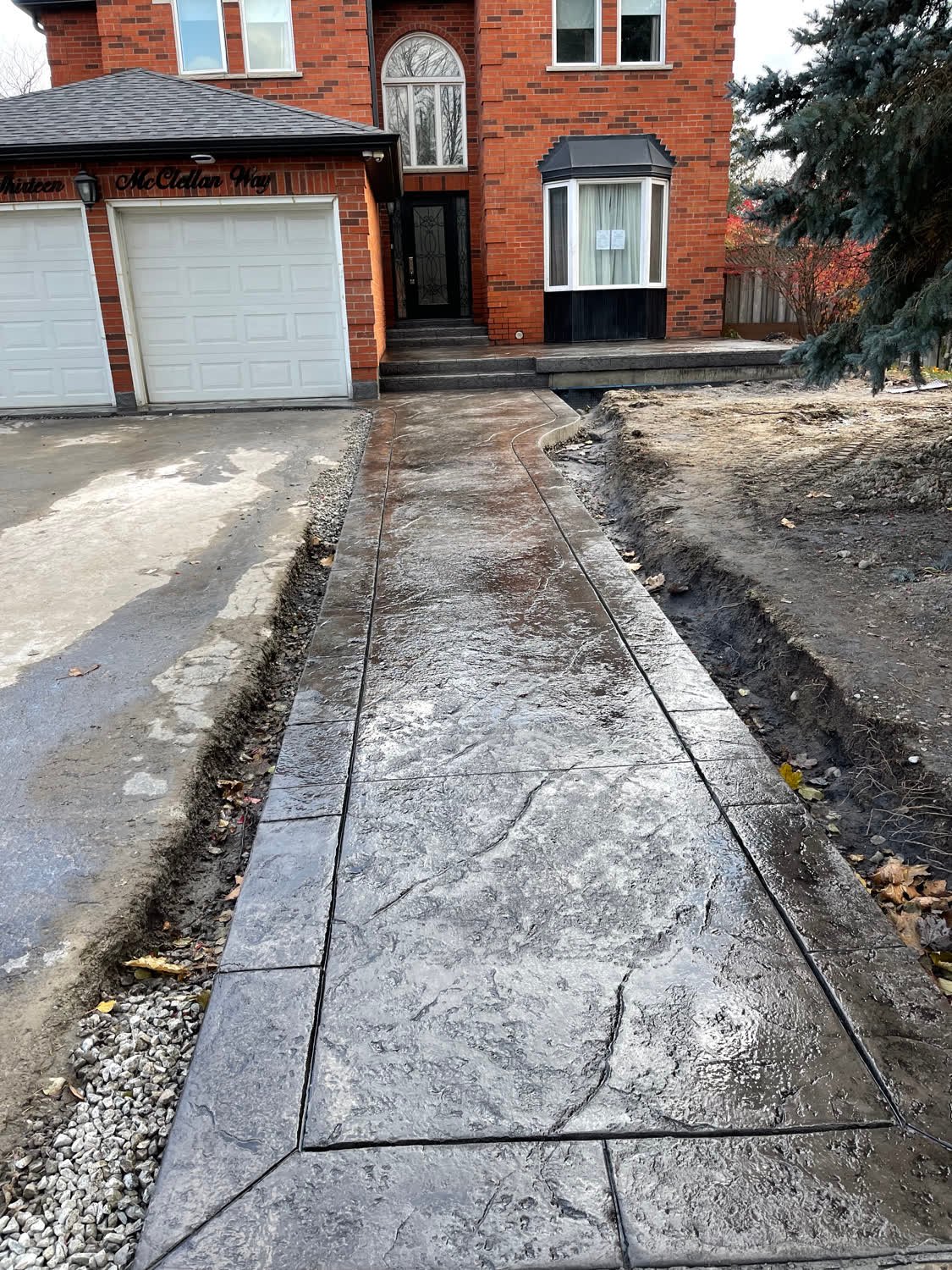 Grey random-stone stamped concrete walkway with a banded border curving from driveway to front door
