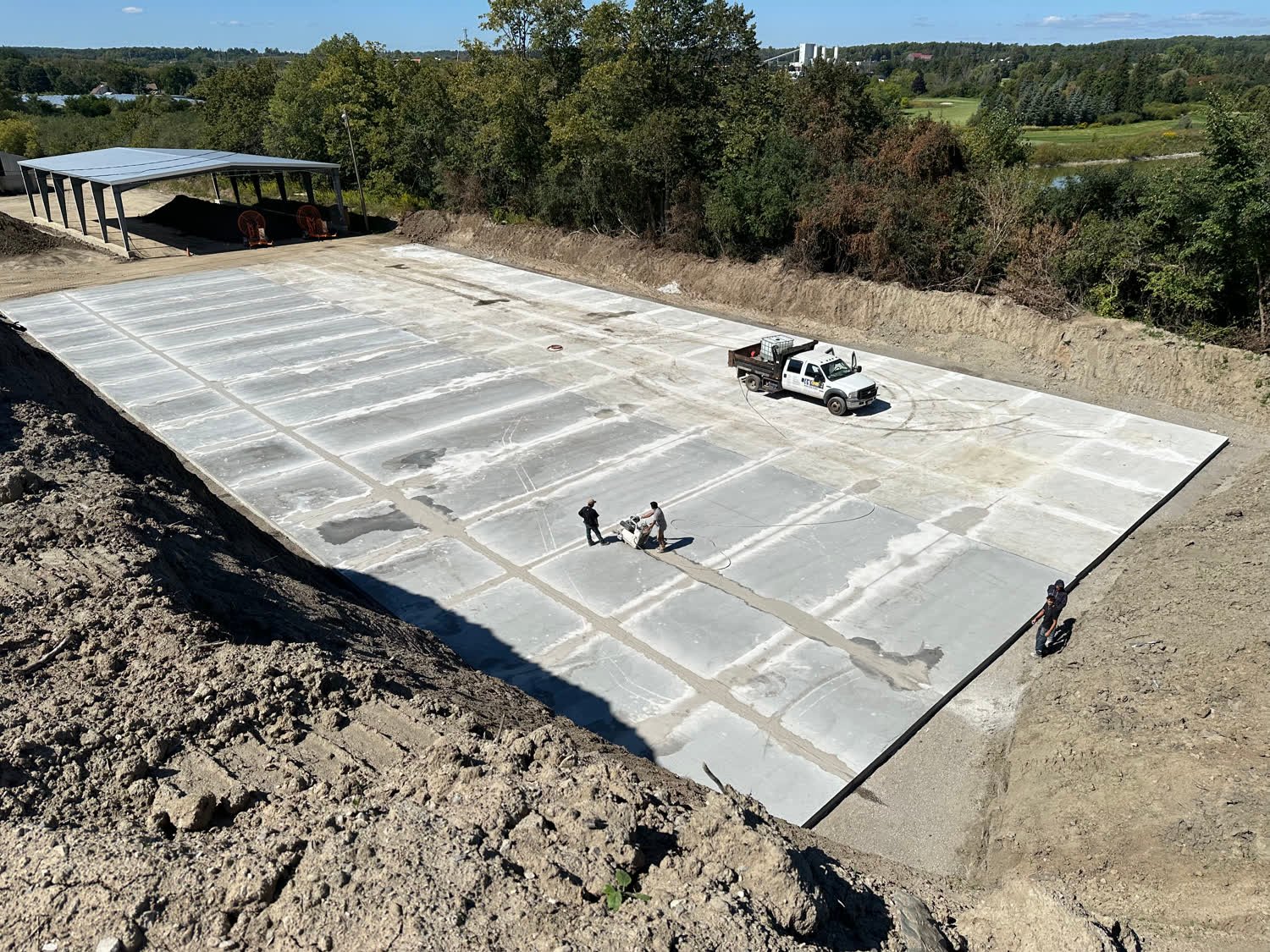 Very large finished concrete yard slab on an engineered base with a truck parked on it and a crew saw-cutting joints